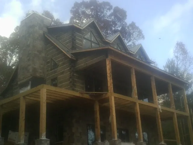 Stone chimney and dormers on a large log home with a timber porch in New London